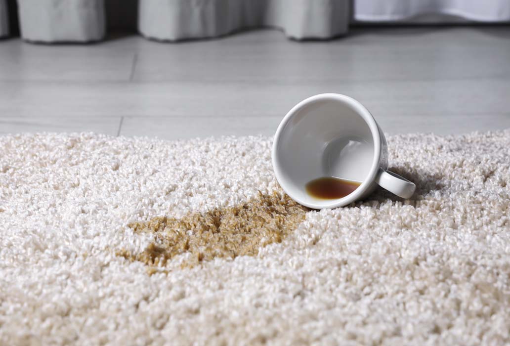 Chávena entornada e mancha de café num tapete claro